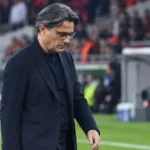 Vincenzo Montella in een donkere jas naast de technische zone van een voetbalstadion.