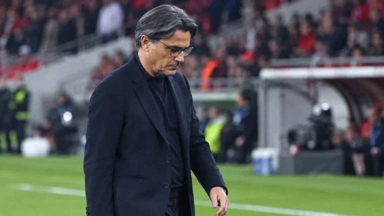 Vincenzo Montella in een donkere jas naast de technische zone van een voetbalstadion.