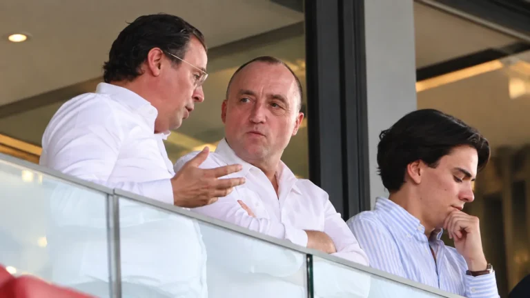 Drie niet-spelende clubvertegenwoordigers in een stadionloge tijdens een gesprek.
