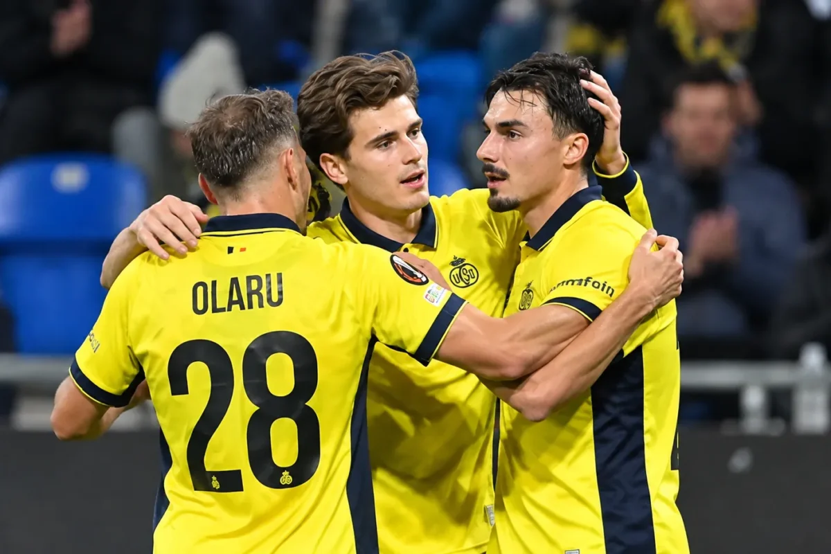 Drie spelers van Union Saint-Gilloise vieren samen op het veld in gele shirts.