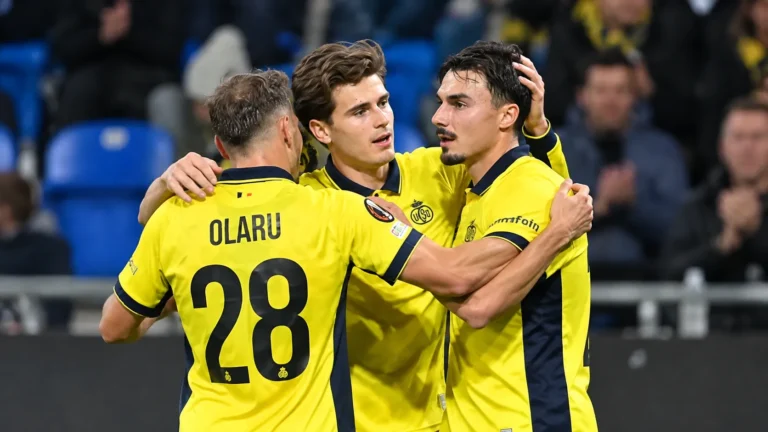 Drie spelers van Union Saint-Gilloise vieren samen op het veld in gele shirts.