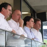 Een groep clubofficials in een stadionloge tijdens een voetbalwedstrijd.