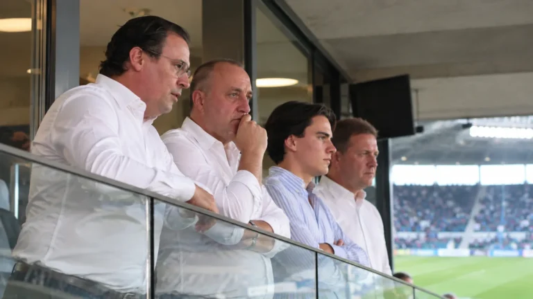 Een groep clubofficials in een stadionloge tijdens een voetbalwedstrijd.