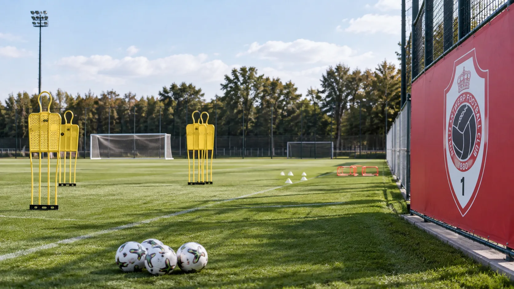 Leeg trainingsveld met verdedigingsmannequins en een vast Royal Antwerp-embleem langs het veld.