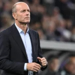 Jess Thorup kijkt aandachtig toe vanaf de zijlijn van een voetbalstadion.