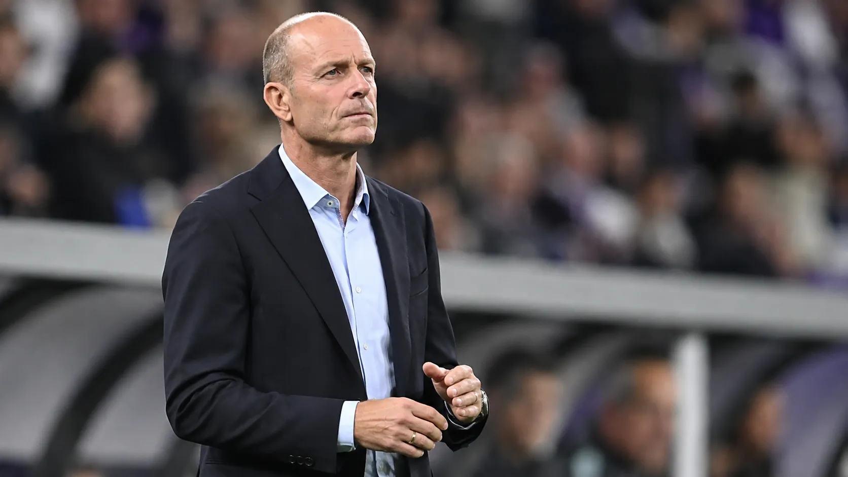 Jess Thorup kijkt aandachtig toe vanaf de zijlijn van een voetbalstadion.