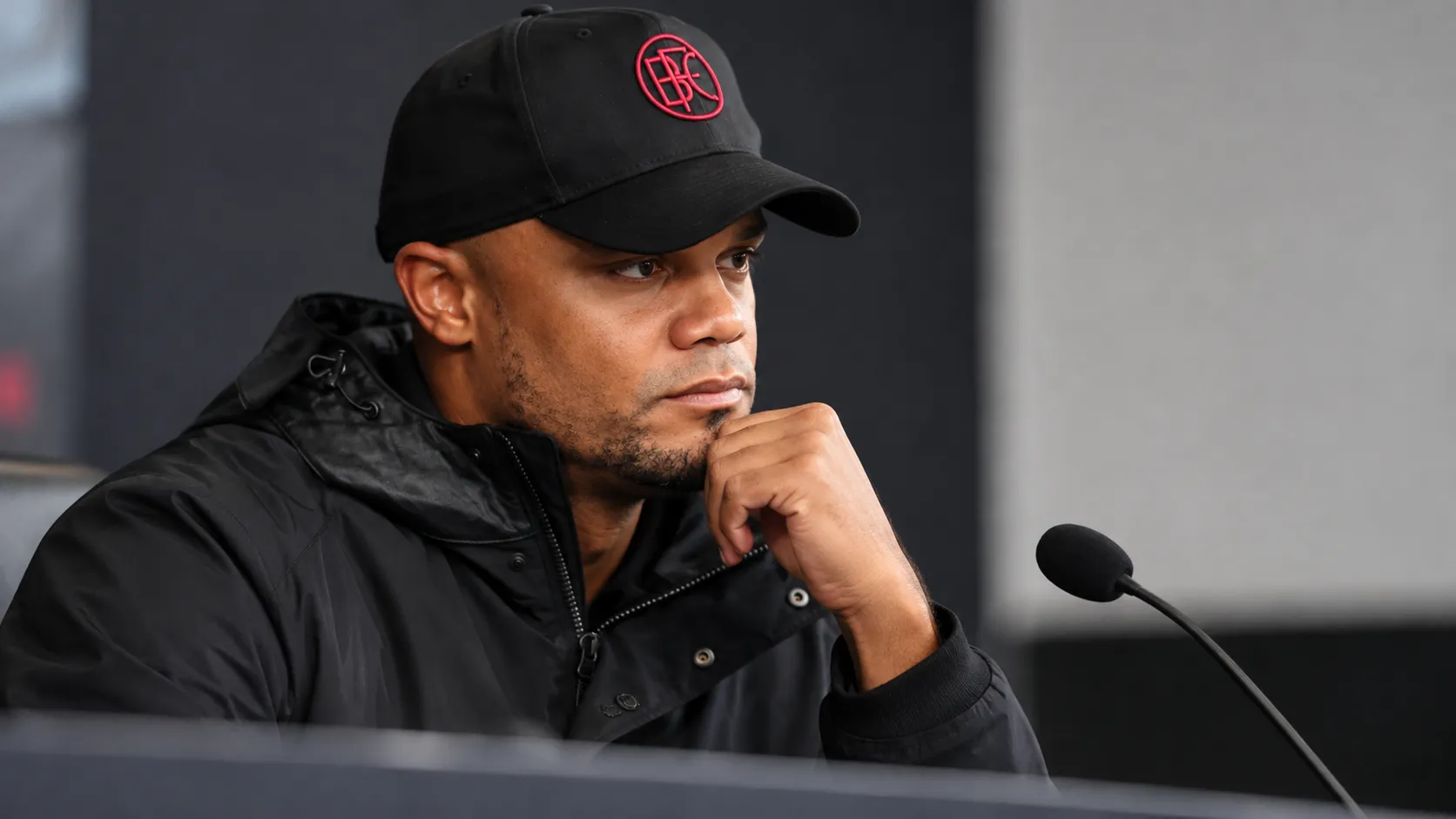 Vincent Kompany in een donkere jas en pet tijdens een rustig mediamoment.