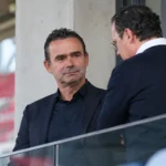 Twee clubofficials in donkere pakken overleggen in een tribunevak van Antwerp.