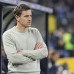 David Hubert in grijze trui langs de zijlijn met een subtiel Union-embleem op de dug-out.