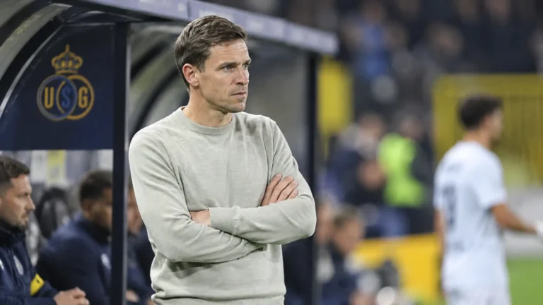 David Hubert in grijze trui langs de zijlijn met een subtiel Union-embleem op de dug-out.