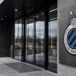 Lege ingang van een Club Brugge-clubgebouw met een clubembleem op een metalen gevelplaat.