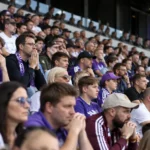 Een volle tribune met aandachtige supporters van RSC Anderlecht in paarse supporterskleding.