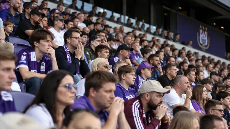 Een volle tribune met aandachtige supporters van RSC Anderlecht in paarse supporterskleding.