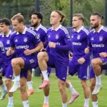 Een groep spelers van RSC Anderlecht warmt op het veld op in paarse wedstrijdtenues.