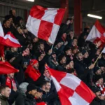 Een groep KV Kortrijk-supporters zwaait met rood-witte vlaggen op de tribune.