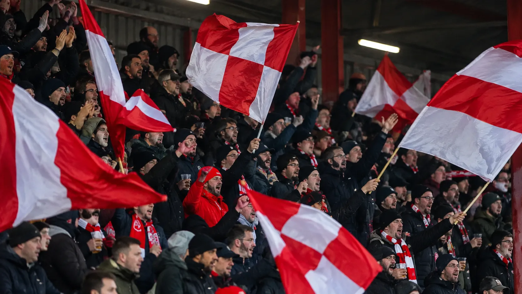 Een groep KV Kortrijk-supporters zwaait met rood-witte vlaggen op de tribune.