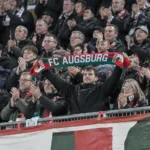 Collectieve supporters van Augsburg vieren in de thuistribune met een clubsjaal.