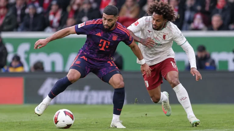 Een speler van Bayern München schermt de bal af terwijl een speler van FC Augsburg druk zet.