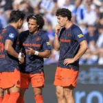 Een groep voetballers in donkerblauwe shirts en oranje broeken op het veld.