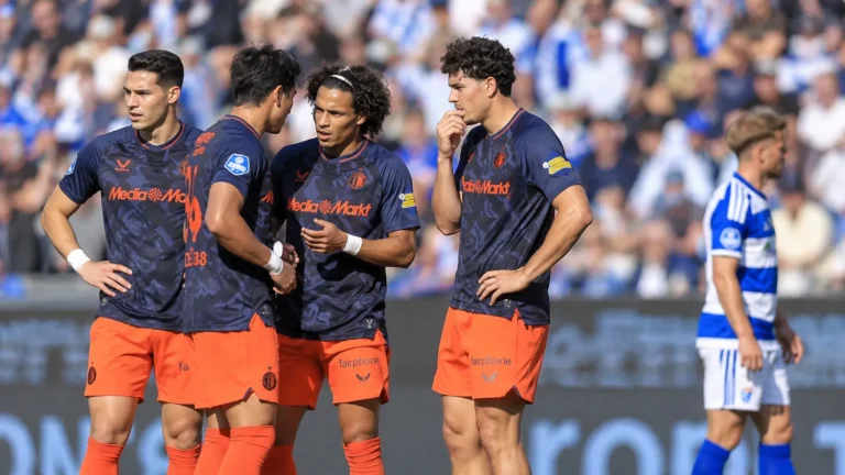 Een groep voetballers in donkerblauwe shirts en oranje broeken op het veld.