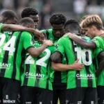 Een groep voetballers in groen-zwarte tenues vormt na de wedstrijd een hechte kring op het veld.