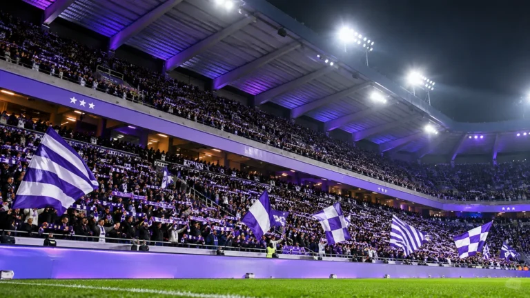 Paars-witte supporters met vlaggen in een verlichte stadiontribune van RSC Anderlecht.