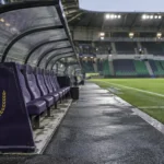 Lege technische zone van RSC Anderlecht na een uitwedstrijd, met een clubembleem op het vaste dug-outpaneel.