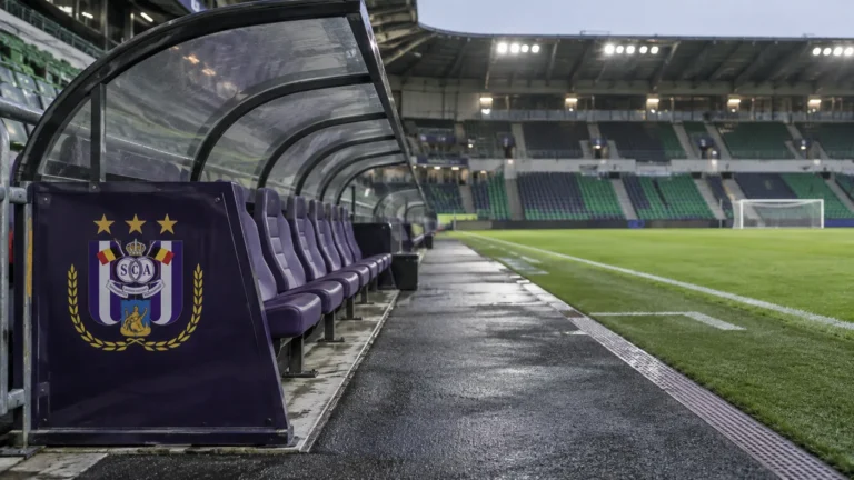 Lege technische zone van RSC Anderlecht na een uitwedstrijd, met een clubembleem op het vaste dug-outpaneel.