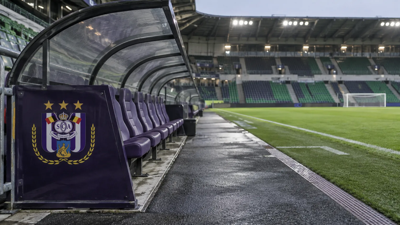 Lege technische zone van RSC Anderlecht na een uitwedstrijd, met een clubembleem op het vaste dug-outpaneel.