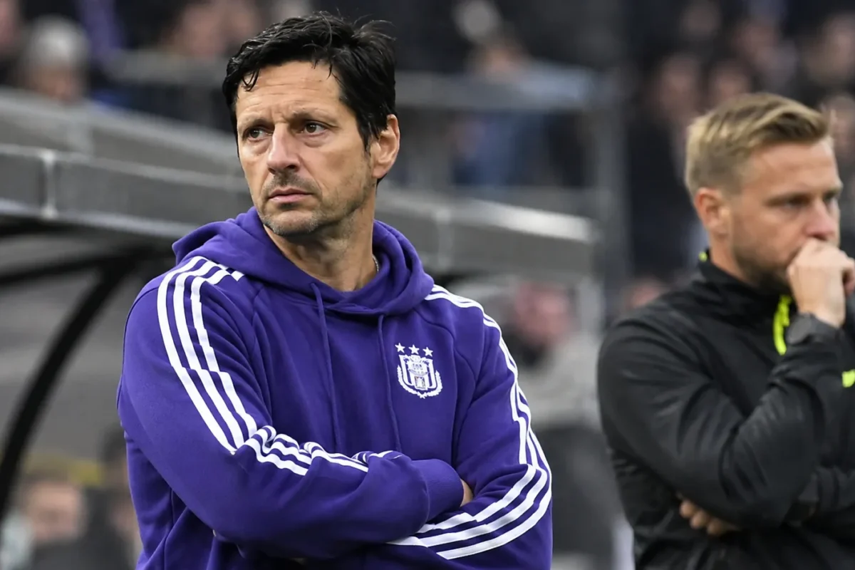 Twee leden van de technische staf van Anderlecht kijken langs de zijlijn naar het veld.