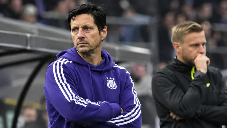 Twee leden van de technische staf van Anderlecht kijken langs de zijlijn naar het veld.