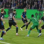 Voetballers in een zwart-blauw en groen tenue tijdens een duel in het strafschopgebied.