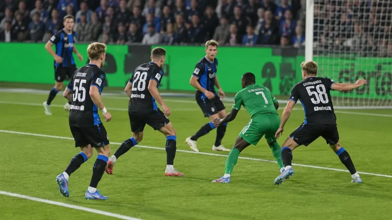 Voetballers in een zwart-blauw en groen tenue tijdens een duel in het strafschopgebied.
