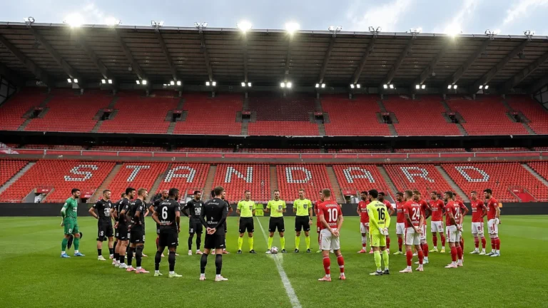 Spelers en scheidsrechters staan opgesteld voor lege rode tribunes in Sclessin.