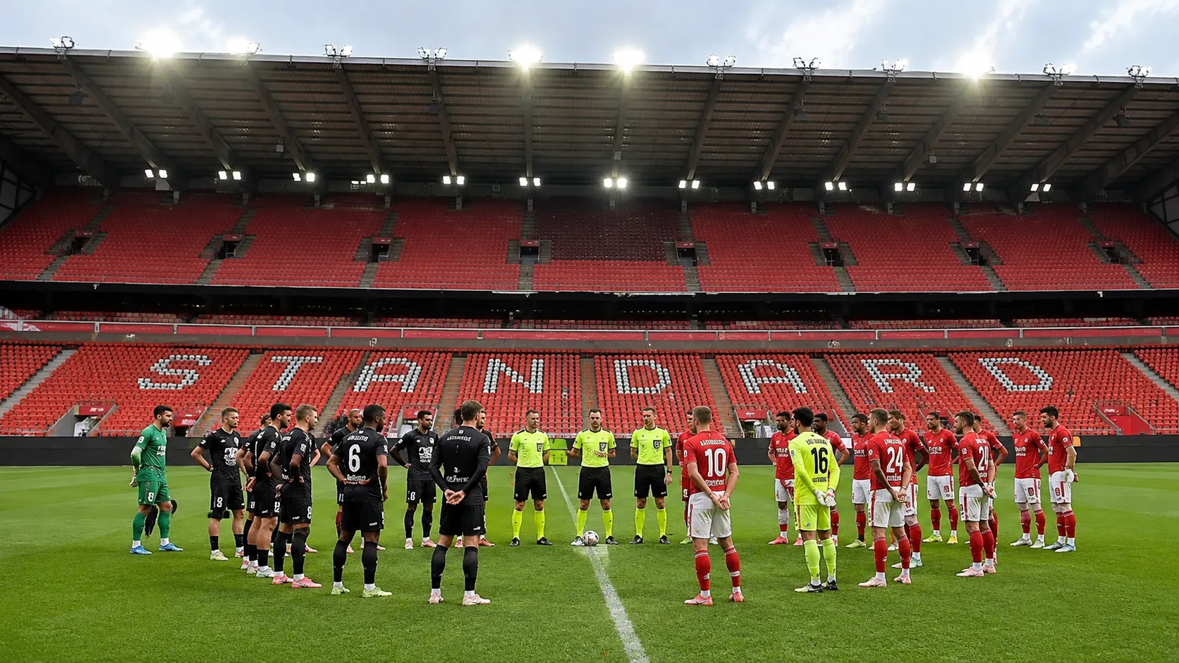 Spelers en scheidsrechters staan opgesteld voor lege rode tribunes in Sclessin.