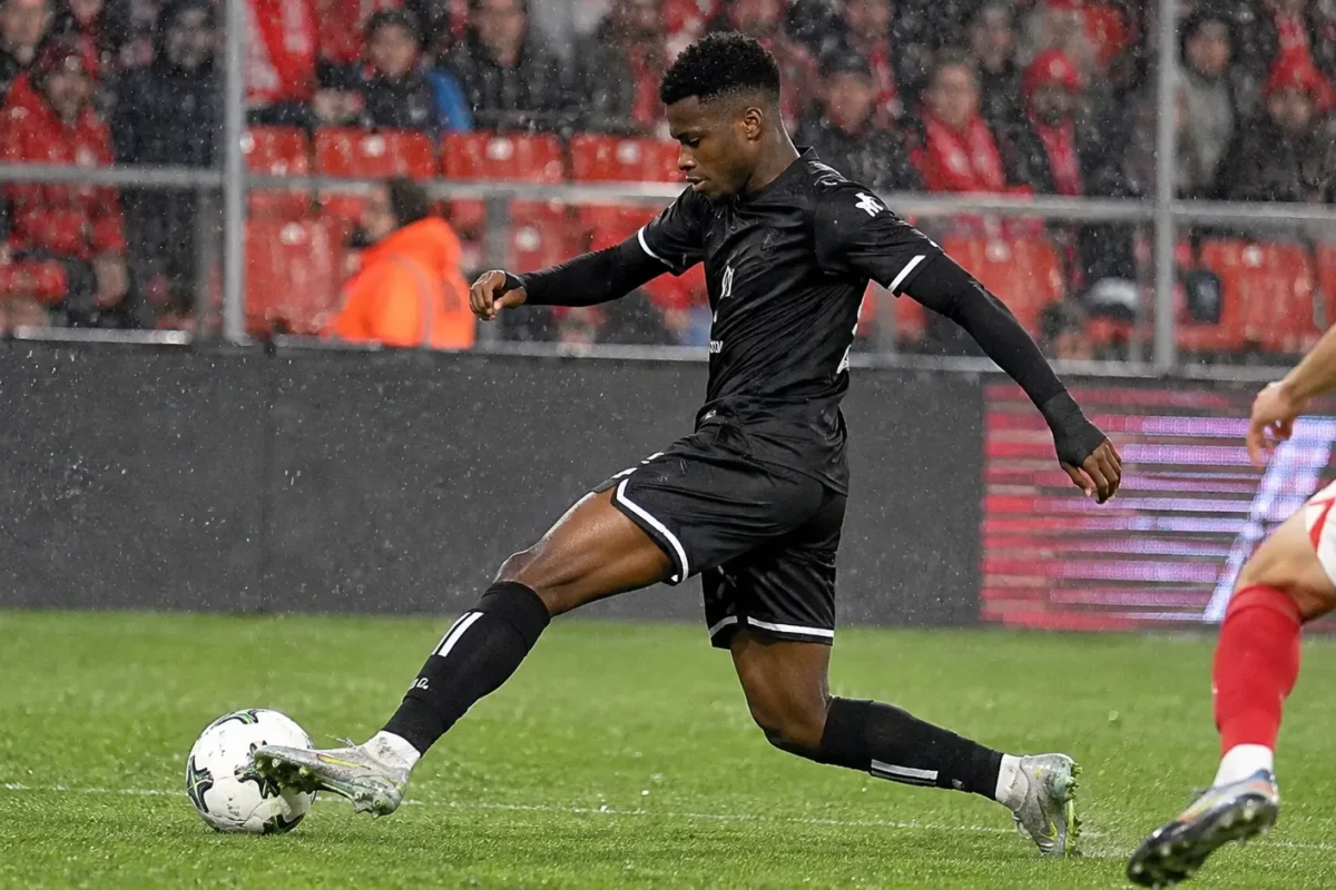 Een voetballer in een zwart wedstrijdtenue tijdens een duel in Sclessin.