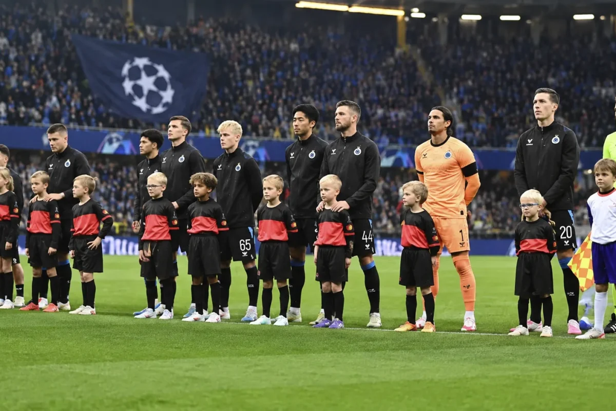 Club Brugge-spelers in zwarte wedstrijdjassen tijdens een Europese wedstrijdopstelling op het veld.