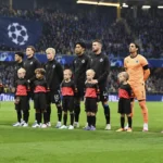 Club Brugge-spelers in zwarte wedstrijdjassen tijdens een Europese wedstrijdopstelling op het veld.