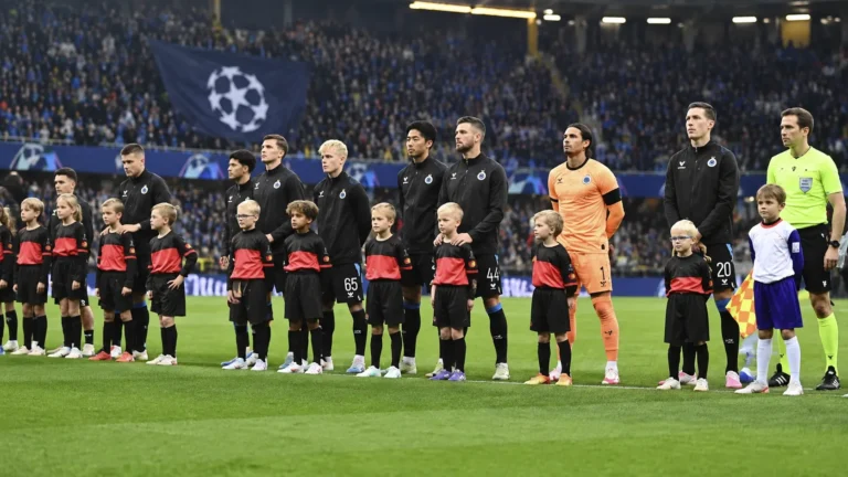 Club Brugge-spelers in zwarte wedstrijdjassen tijdens een Europese wedstrijdopstelling op het veld.