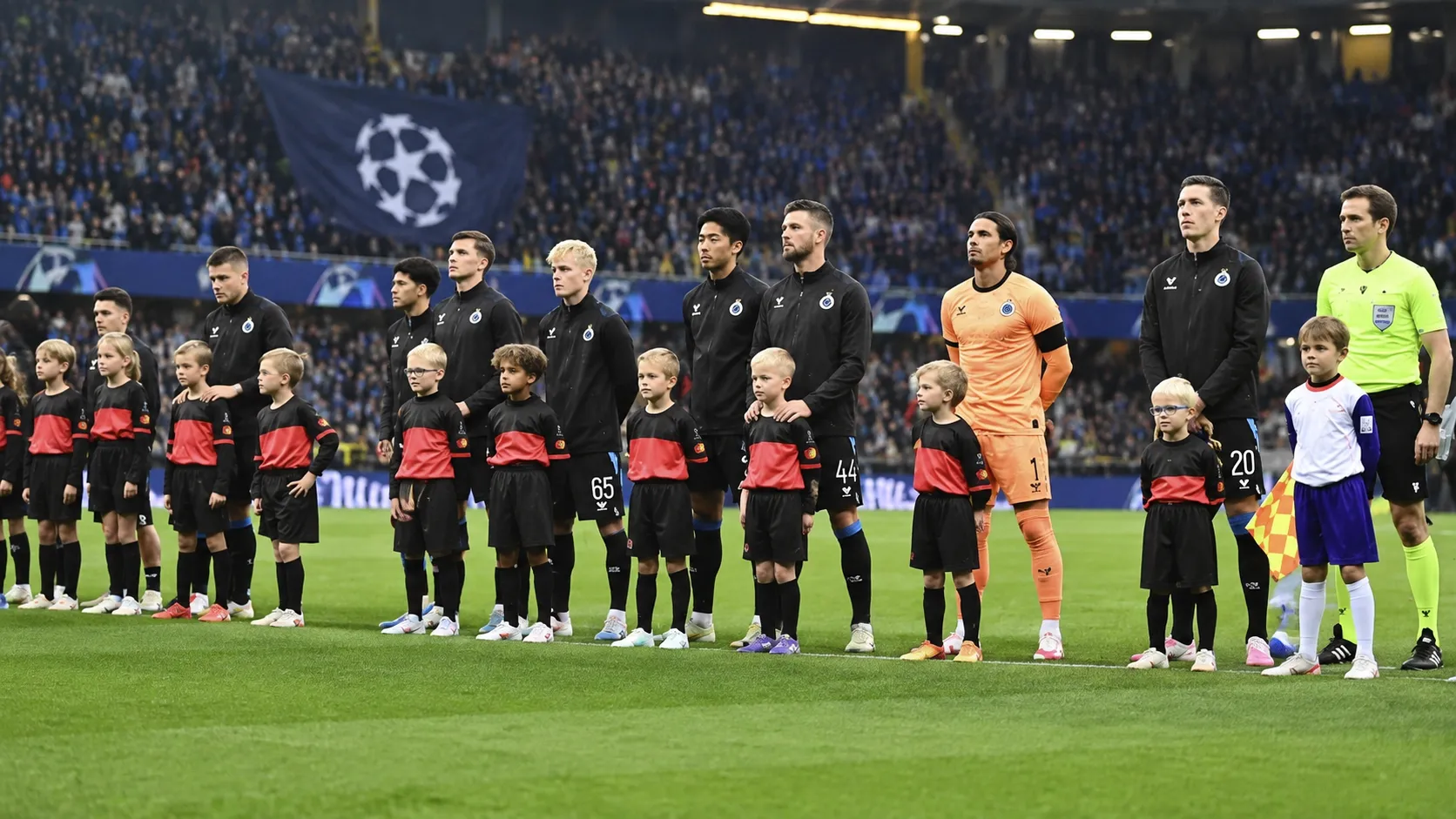 Club Brugge-spelers in zwarte wedstrijdjassen tijdens een Europese wedstrijdopstelling op het veld.