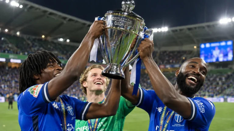 Drie voetballers van South Melbourne vieren met de Australia Cup op het veld.