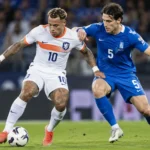 Twee voetballers van Nederland en Griekenland in duel op het veld.