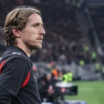 Een AC Milan-speler in zwart-rode sportkleding langs de zijlijn van een stadion.