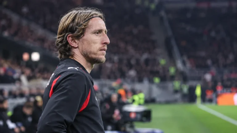 Een AC Milan-speler in zwart-rode sportkleding langs de zijlijn van een stadion.