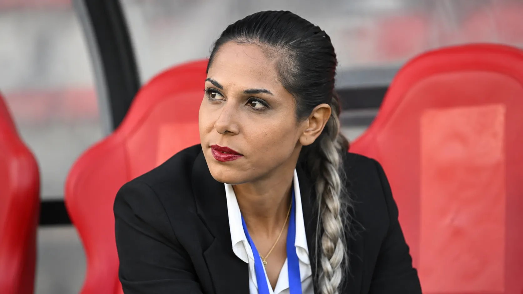 Ster Habibzadeh zit geconcentreerd op een rode stadionbank.