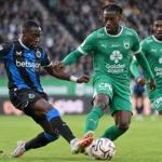 Voetballers in blauw-zwart en groen vechten om de bal tijdens een competitiewedstrijd.