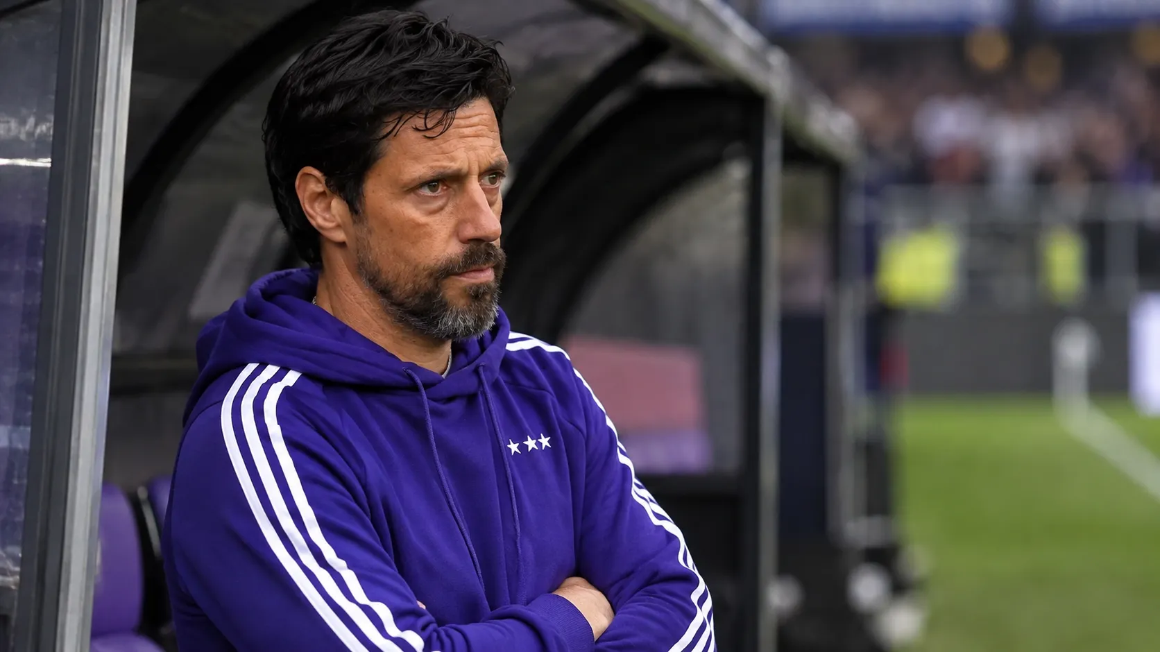 Een Anderlecht-coach kijkt geconcentreerd vanuit de dug-out naar het veld.