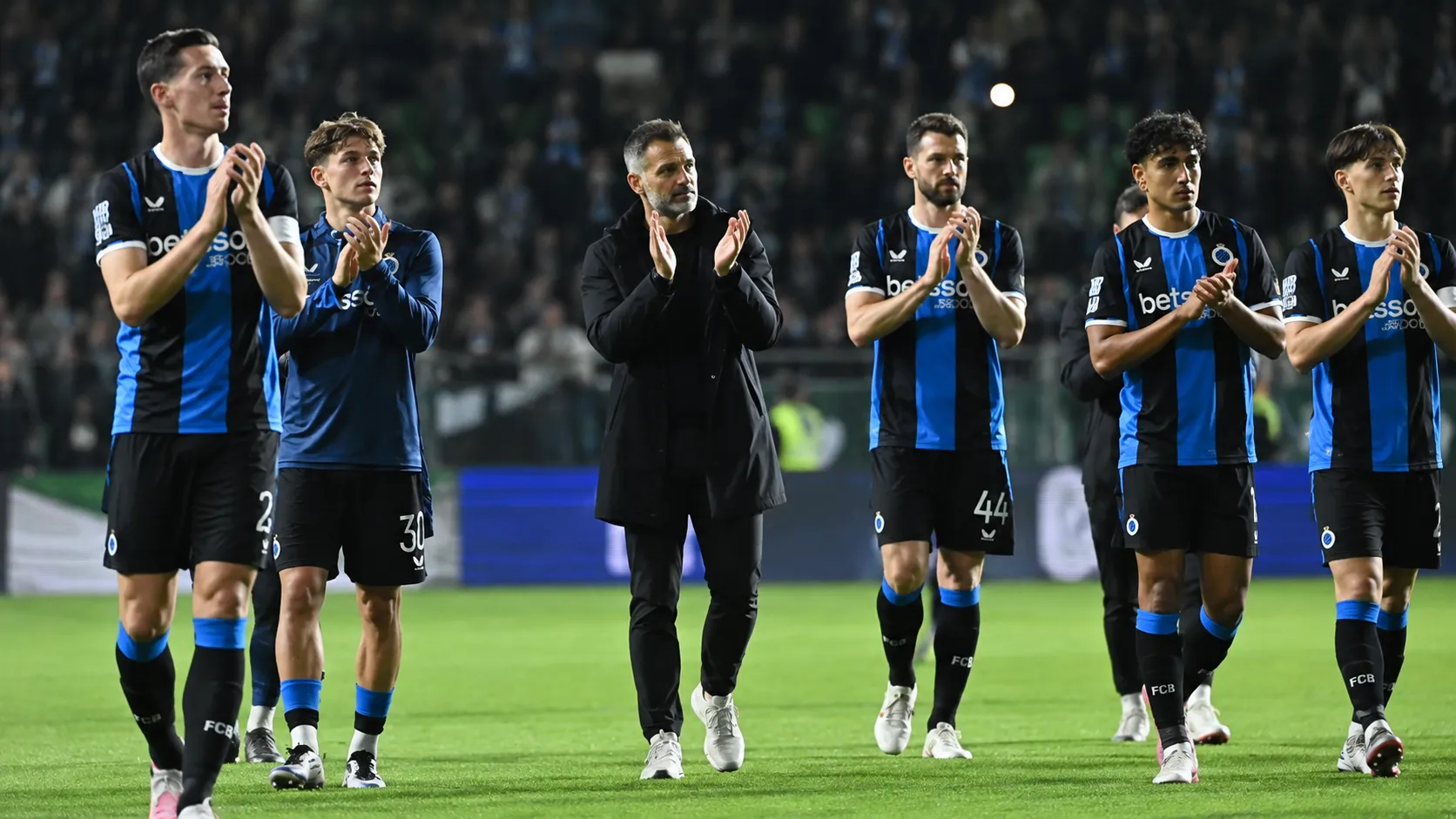 Coach en spelers van Club Brugge applaudisseren na afloop op het veld.