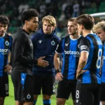 Een groep spelers in zwart-blauwe clubtenues verzamelt zich langs het veld voor een Europese avondwedstrijd.