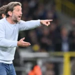 Een coach geeft langs de zijlijn aanwijzingen tijdens een voetbalwedstrijd.